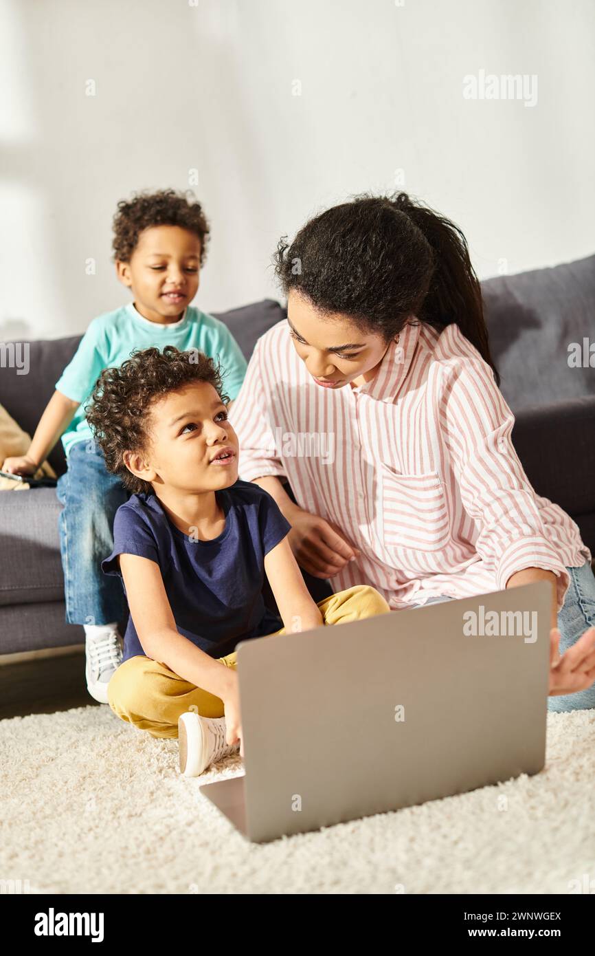 Fröhliche, entzückende afroamerikanische Jungs in Homewear, die Zeit mit ihrer Mutter in der Nähe eines Laptops verbringen Stockfoto