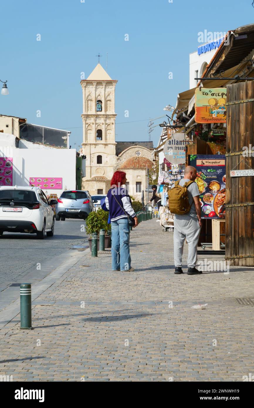 Touristenpaar, das sich Restaurants und Geschäfte mit der St. Lazarus Kirche anschaut. Larnaka, Zypern. Februar 2024 Stockfoto