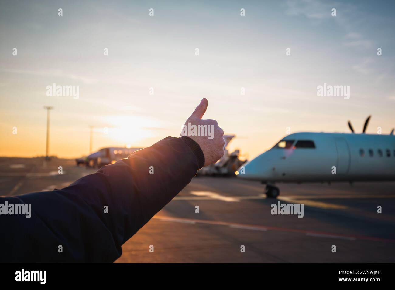 Mitglied der Bodencrew zeigt die Daumen nach oben zum Flugzeug. Verkehr am Flughafen bei Sonnenuntergang. Stockfoto