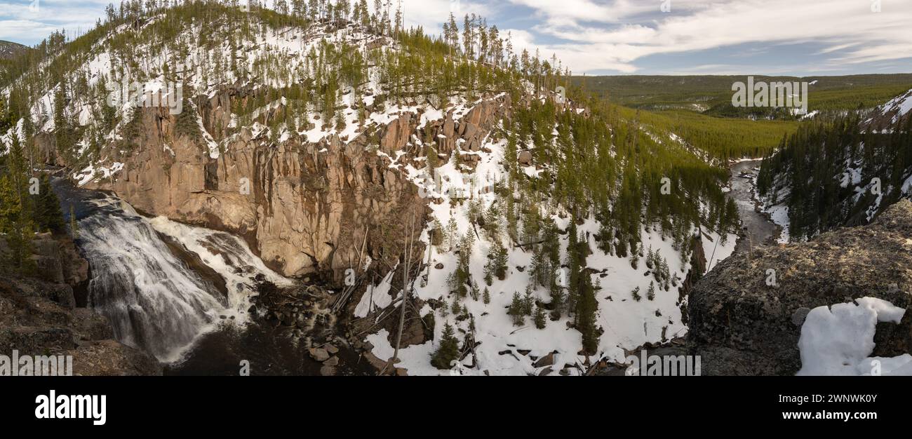 Ein bezauberndes Bild eines mächtigen Wasserfalls, der durch eine schneebedeckte Landschaft stürzt und durch die zerklüfteten Klippen, umgeben von Kiefern, schneidet Stockfoto