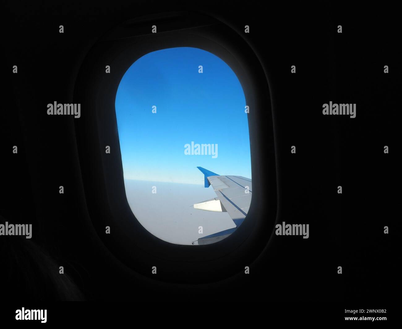 Das Ebenenfenster. Das Bullauge, durch das Sie den Flügel des Flugzeugs, den blauen Himmel, den nebeligen Horizont und die Erde in einem Dunst mit einer Höhe von 10.000 Metern sehen können Stockfoto