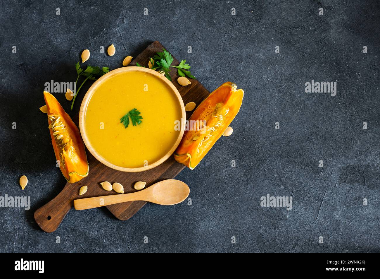Hausgemachte Kürbis-Karottensuppe mit Petersilie in der Schüssel und frischen Kürbissen auf rustikalem Hintergrund Stockfoto
