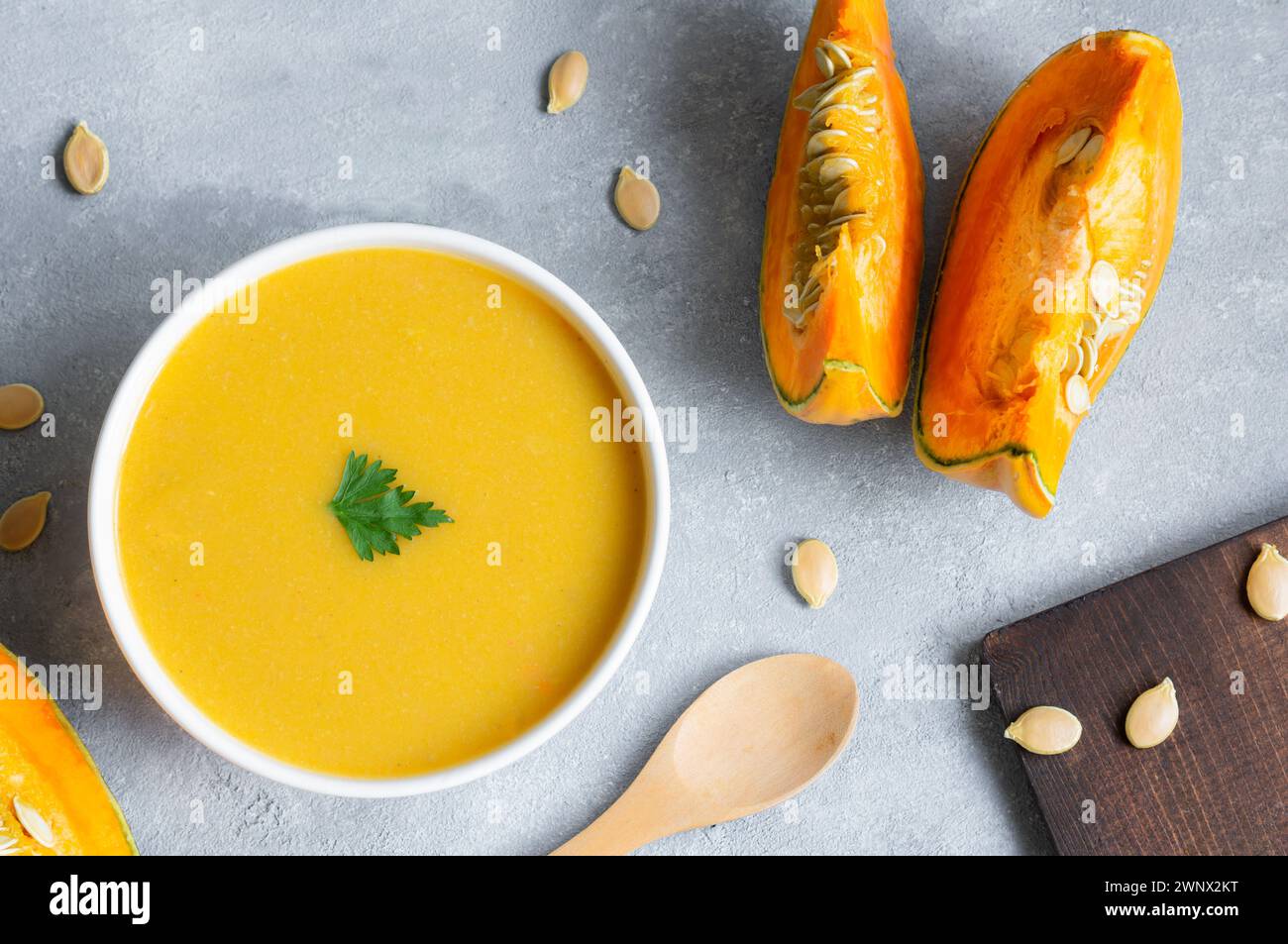 Hausgemachte Kürbis-Karottensuppe mit Petersilie in der Schüssel und frischen Kürbissen auf rustikalem Hintergrund Stockfoto
