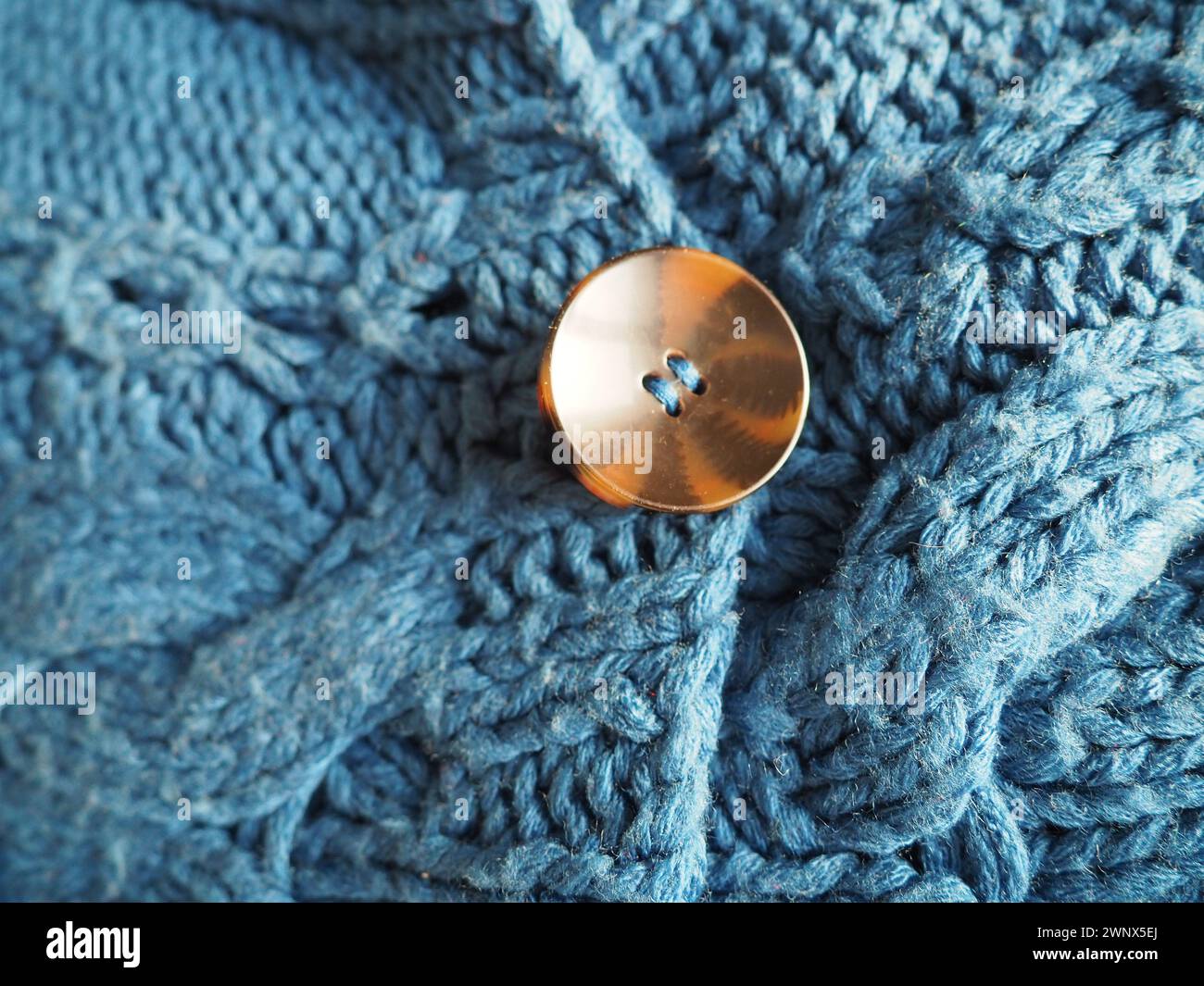 Brauner Kunststoffknopf, mit Gewinde genäht. Der Knopf ist an einem blauen Wollpullover oder Pullover geknöpft. Warme Winterbekleidung für Damen Stockfoto