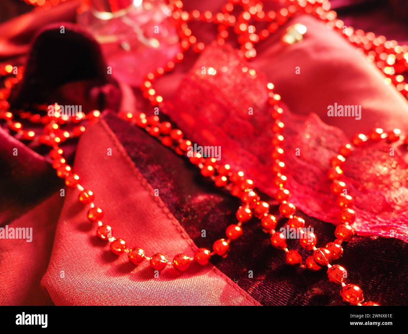 Rote, schöne Perlen auf hellem Scharlachsamt. Schöner luxuriöser Damenschmuck auf weichem Stoff. Flach liegend in Nahaufnahme. Damenkram und Kosmetik Stockfoto