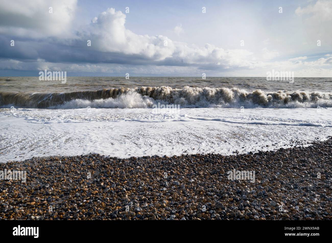 Farbe starkes Sonnenlicht von Wellen, die auf Kieselstrand Brandung, Spume & Spray brechen, grünes Meer, ein blauer Himmel mit wehenden weißen Wolken Südküste Englands Stockfoto