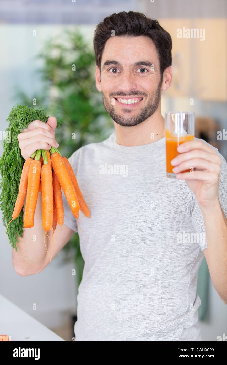 Junger bärtiger Mann trinkt frisch gepressten natürlichen Karottensaft Stockfoto