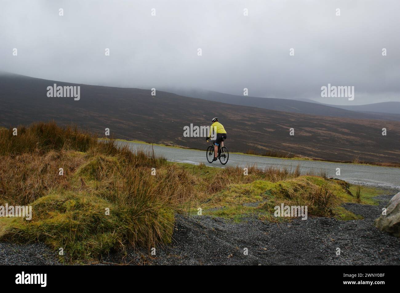 Ein Radfahrer, der auf einer Straße in einem bergigen Gebiet fährt. Landschaft in Irland. Stockfoto