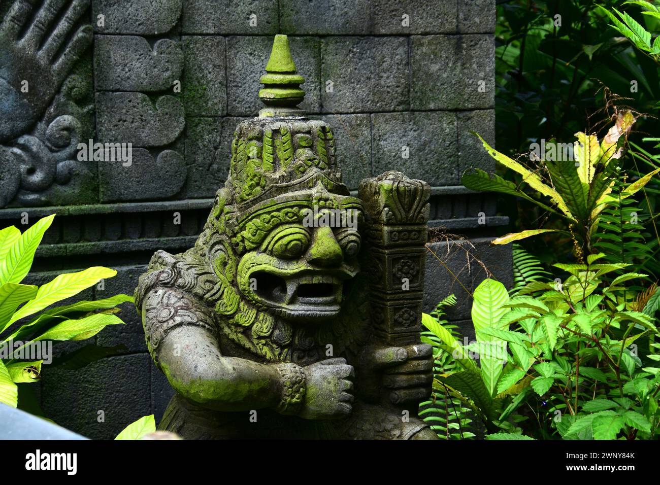 Singapur, 26. Januar 2024. Balinesisch geschnitzte Steinstatue von Rakasa bedeckt mit grünem Moos in einem öffentlichen Park. Stockfoto