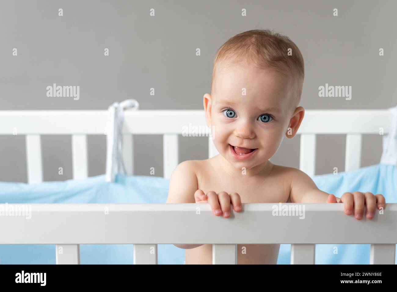 Das Baby sieht vertrauensvoll und freundlich aus, während es in einem Kinderbett steht Stockfoto