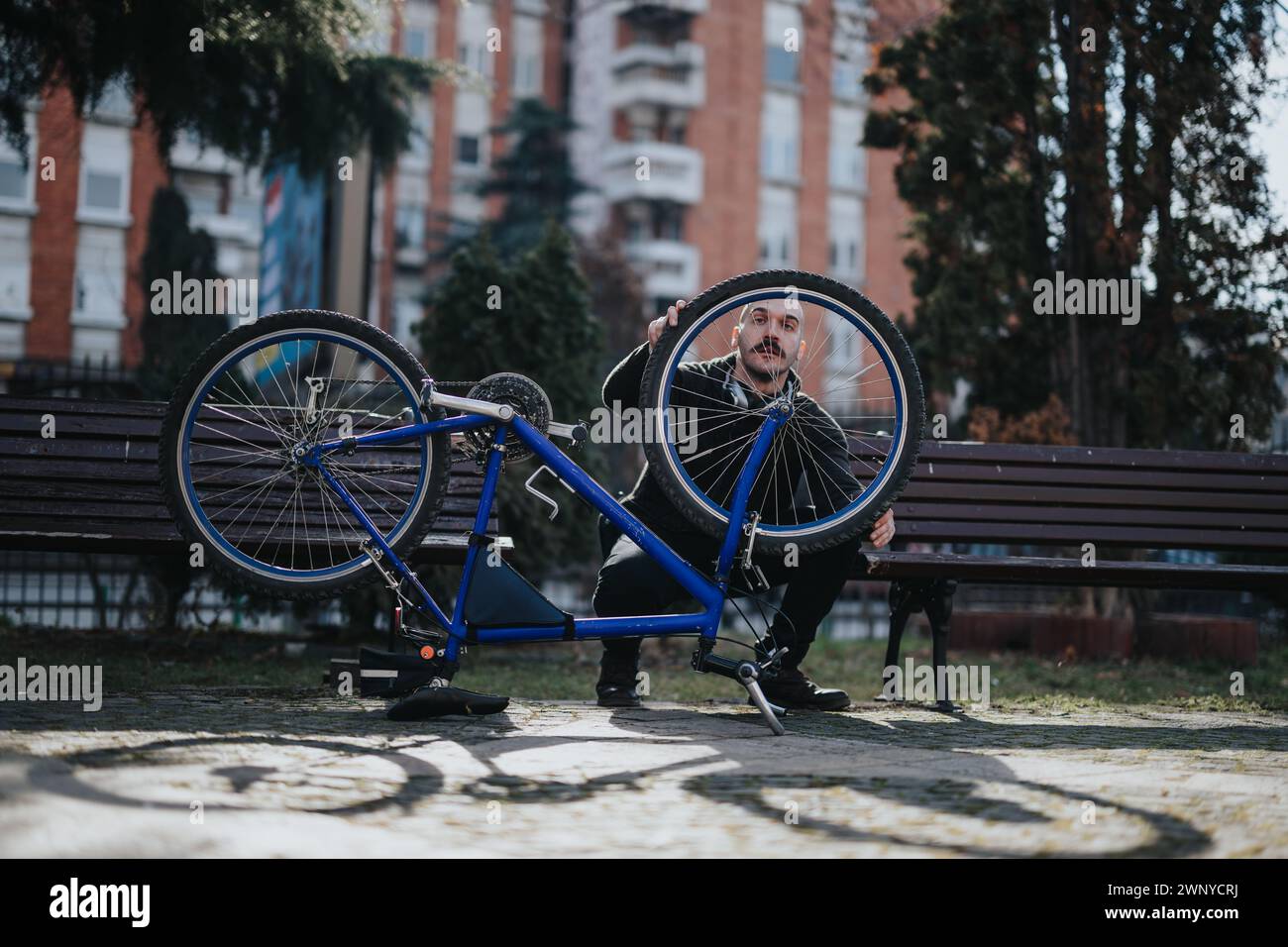 Ein Mann, der Fahrradreparaturen in einem Park mit urbanem Hintergrund durchführt Stockfoto