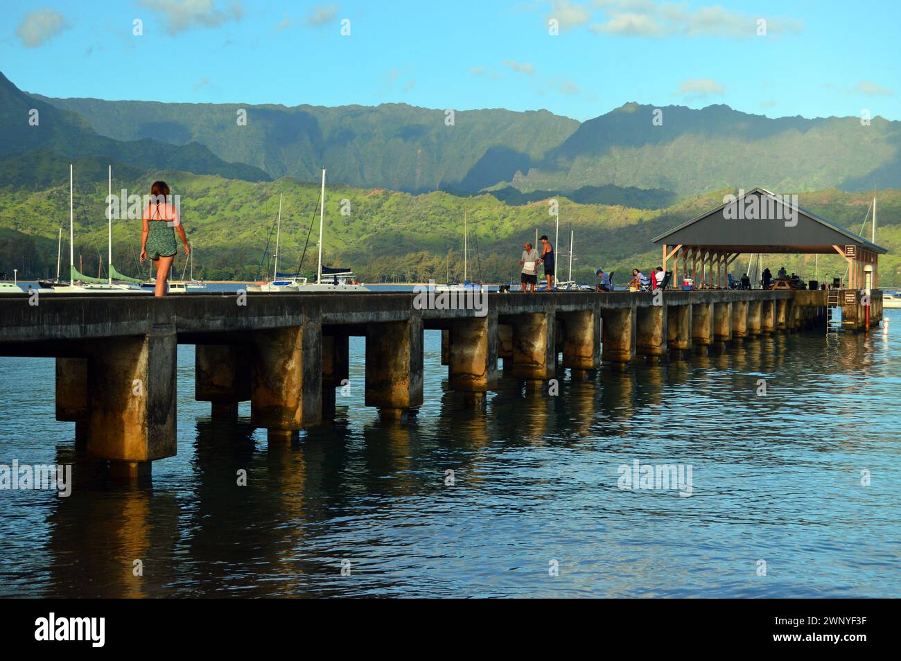 Die Leute spazieren auf dem Pier in der Hanalei Bay, umgeben von den Bergen von Kauai Stockfoto