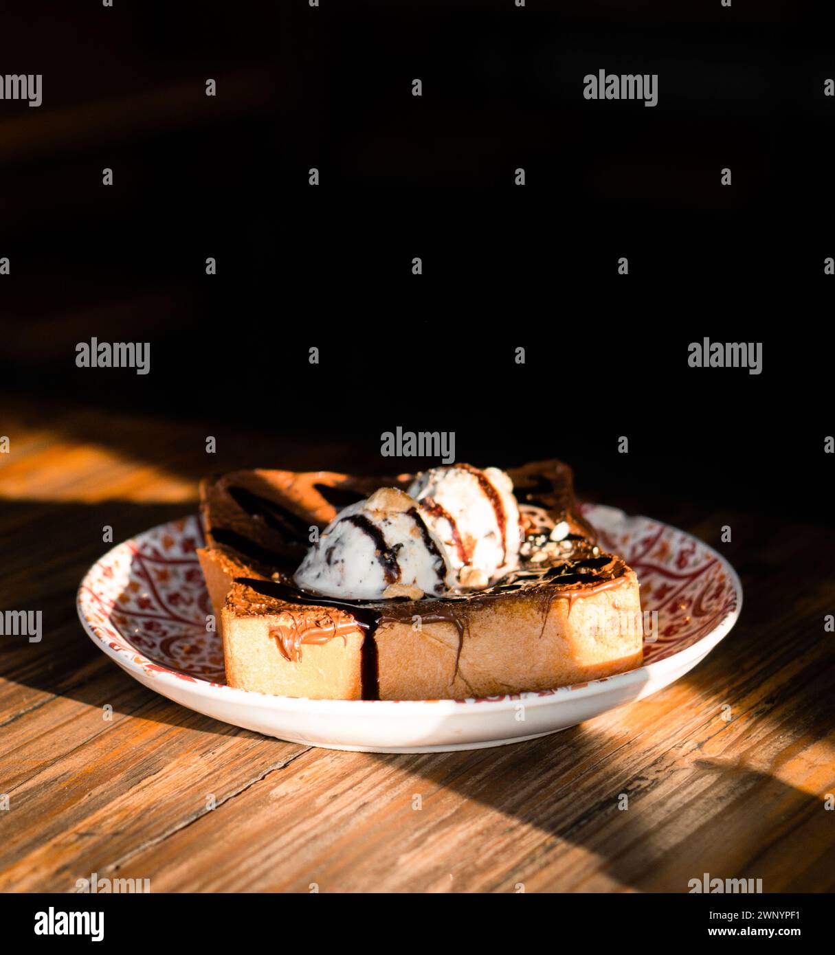Diagonal geschnittener Toast mit Schokoladensauce und Vanilleeis, serviert auf einem roten Teller Stockfoto