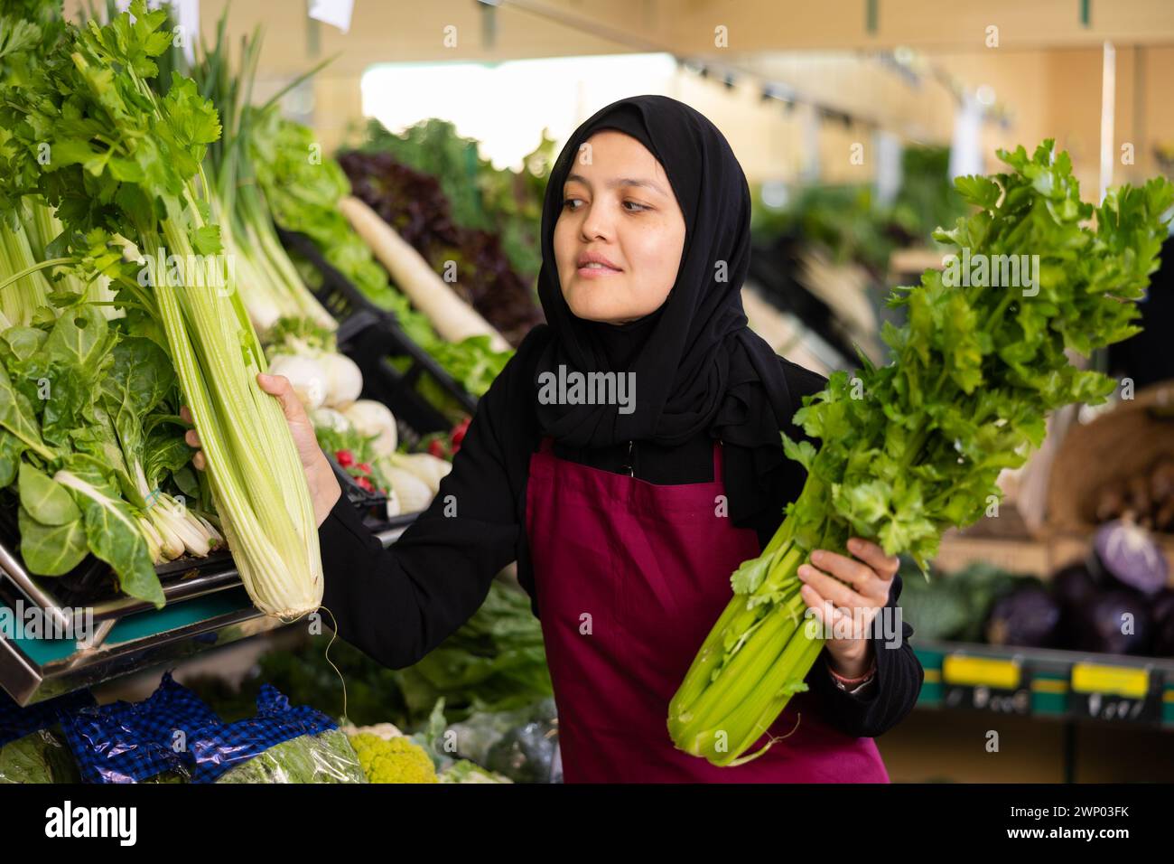 Muslimische Verkäuferin in Schürze nimmt Sellerieblätter aus dem Fenster Stockfoto