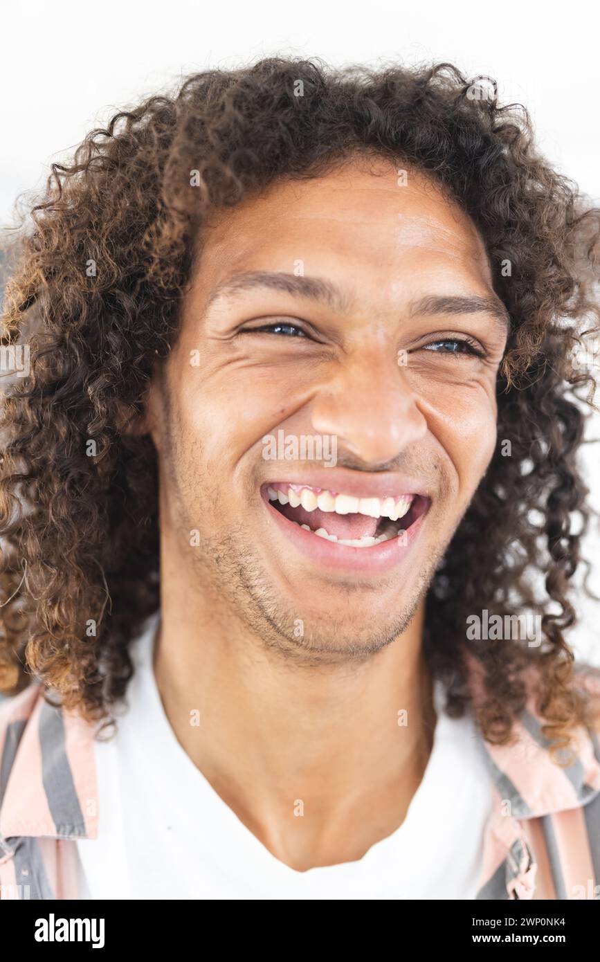 Junger birassischer Mann mit lockigen Haaren lacht fröhlich und zeigt eine positive Stimmung Stockfoto