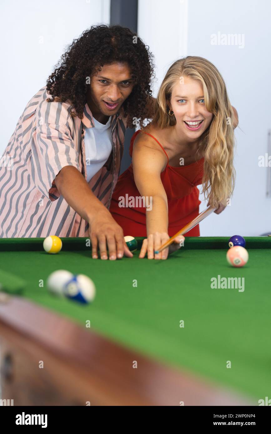 Ein birassischer Mann bringt einer kaukasischen Frau Billard bei, beide lächeln Stockfoto
