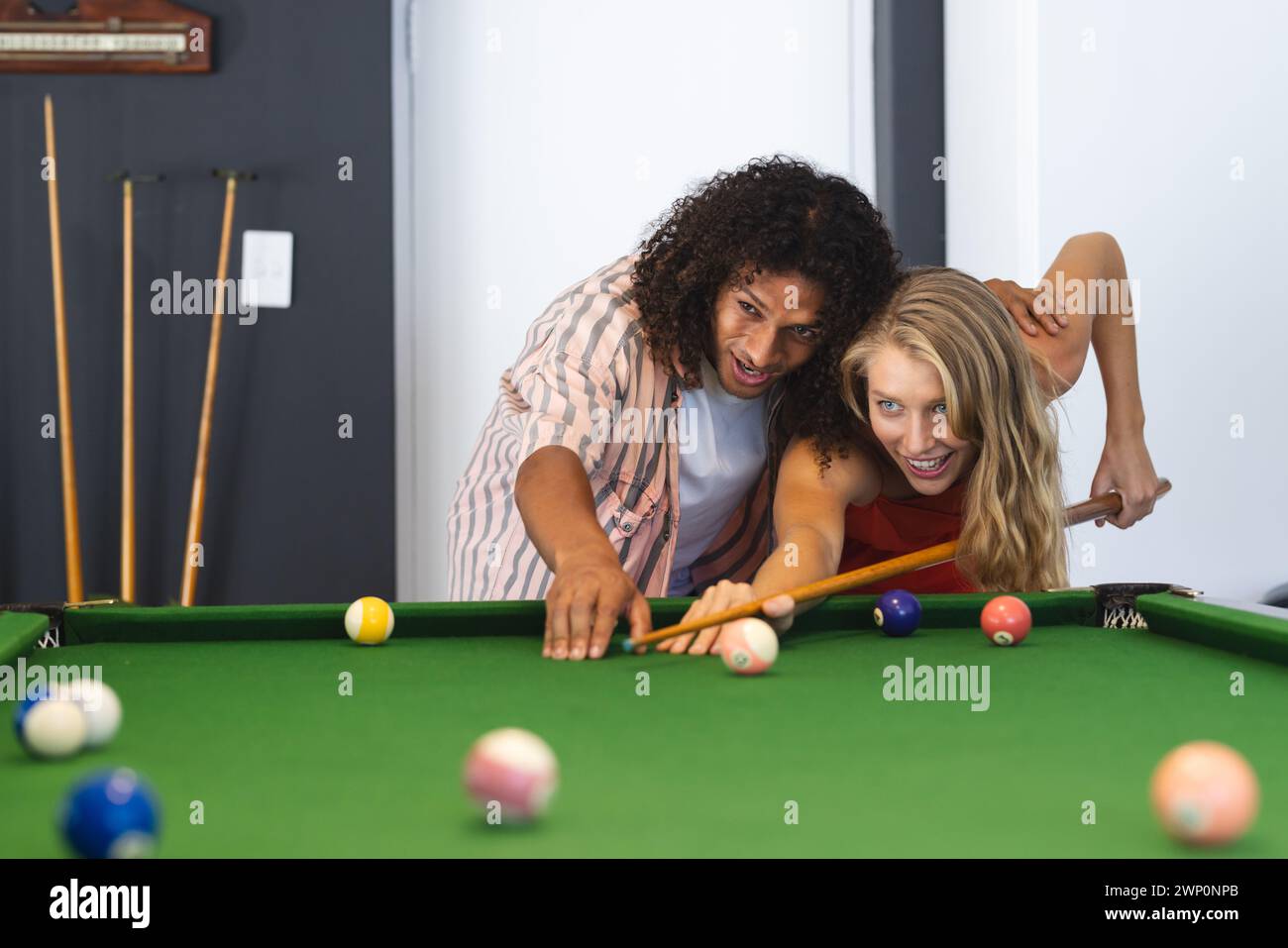 Ein birassischer Mann bringt einer kaukasischen Frau Billard bei, beide lächeln Stockfoto