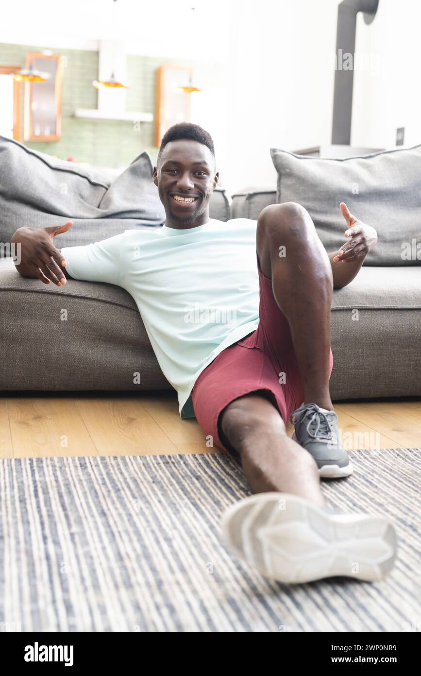 Junger Afroamerikaner in lässiger Kleidung sitzt auf dem Boden und lächelt in die Kamera Stockfoto