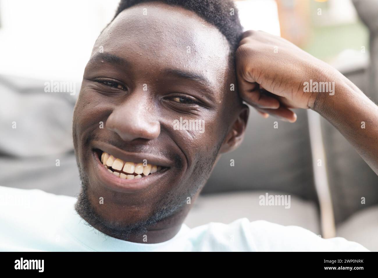 Junger afroamerikanischer Mann mit einem hellen Lächeln, der seine Hand auf dem Kopf hält Stockfoto