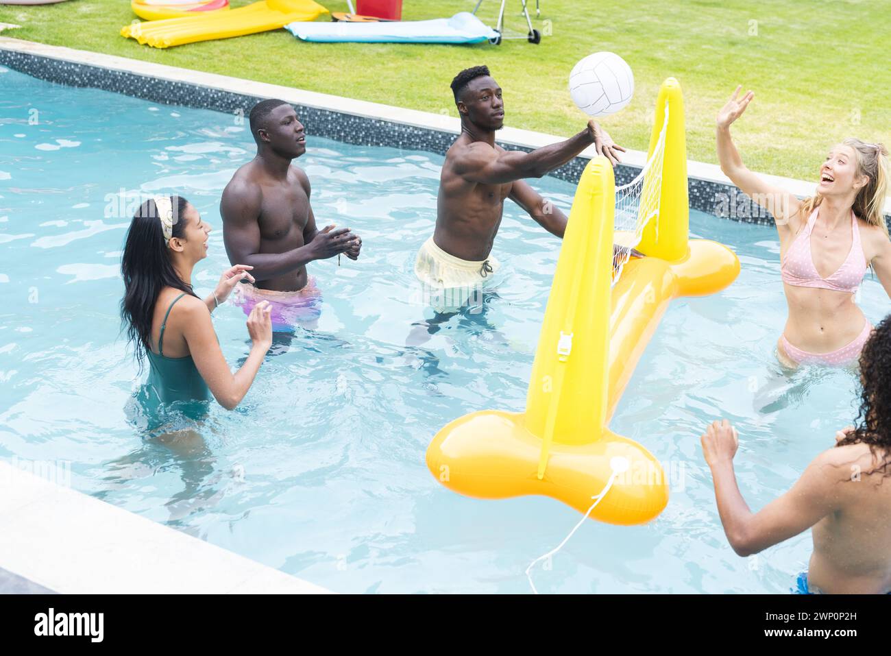 Verschiedene Gruppen von Freunden genießen eine Runde Volleyball in einem Pool, mit einem gelben aufblasbaren in der Nähe Stockfoto