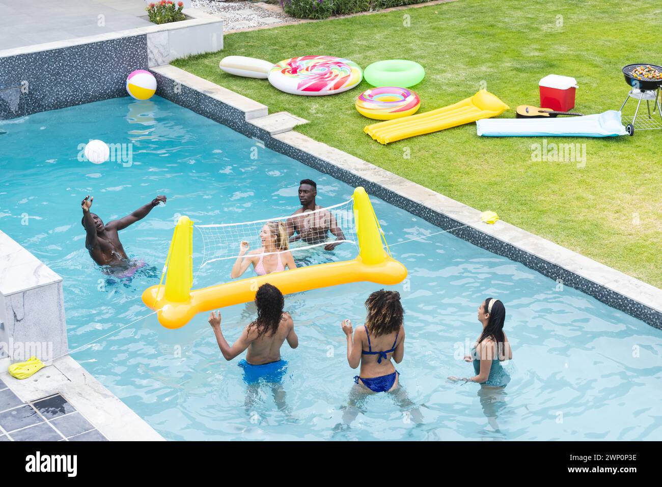 Verschiedene Freunde spielen eine Runde Billardvolleyball, mit farbenfrohen Wagen in der Nähe Stockfoto