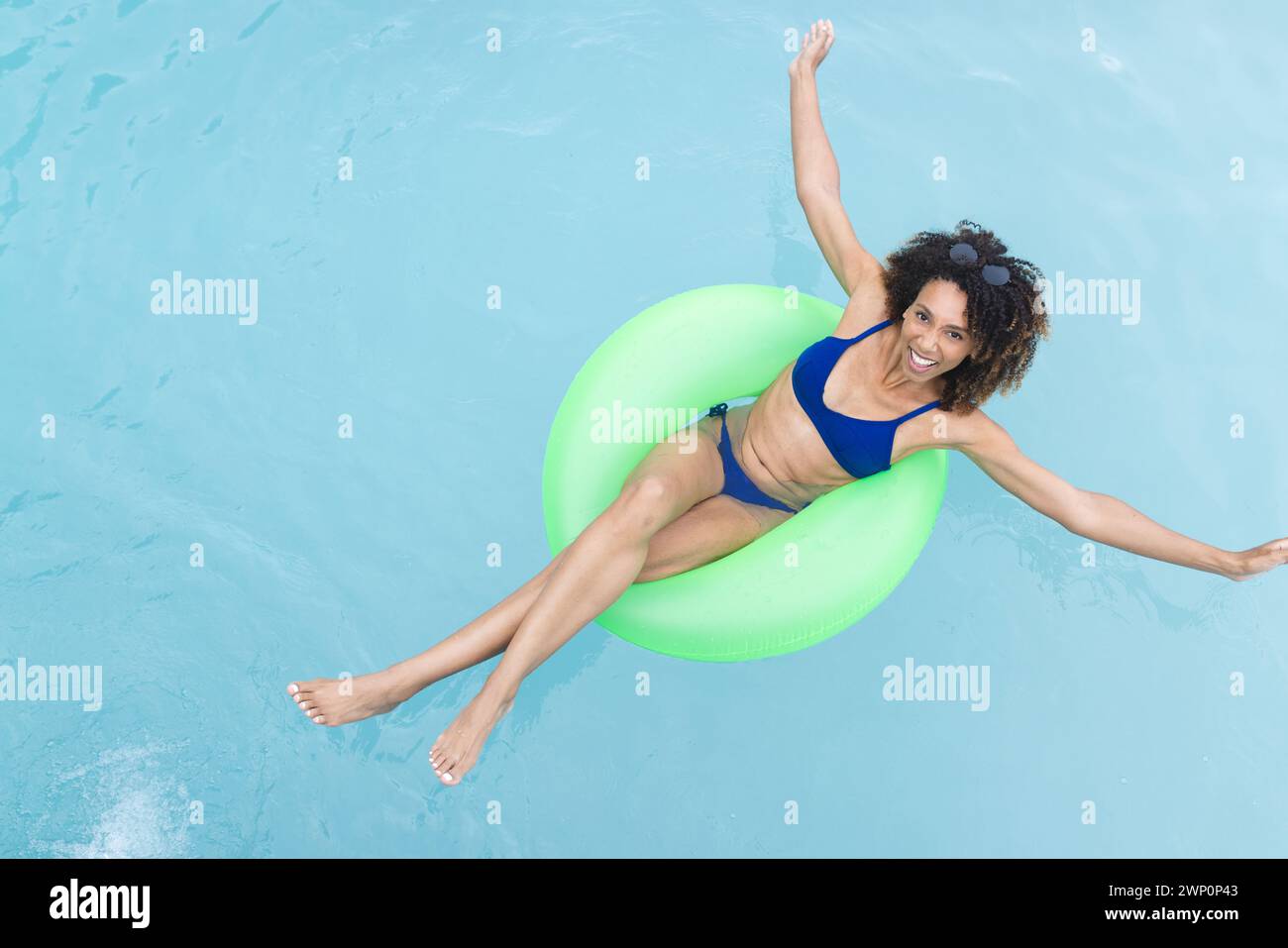 Birassische Frau schwebt gern in einem Pool auf einer grünen Innenröhre und lächelt in die Kamera Stockfoto