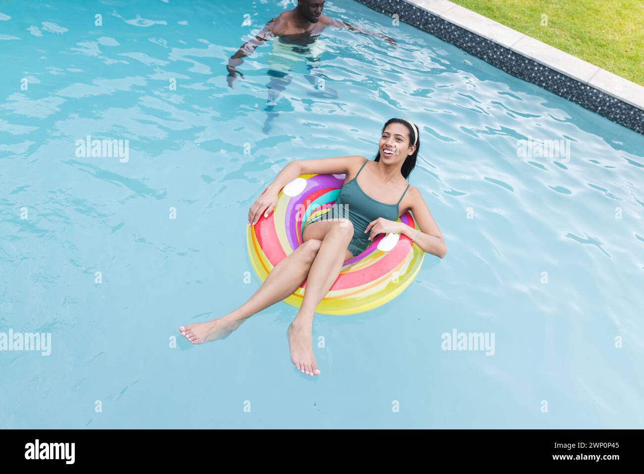Eine junge Frau, die sich auf einem farbenfrohen Schwimmbecken aufhält, lächelt Stockfoto
