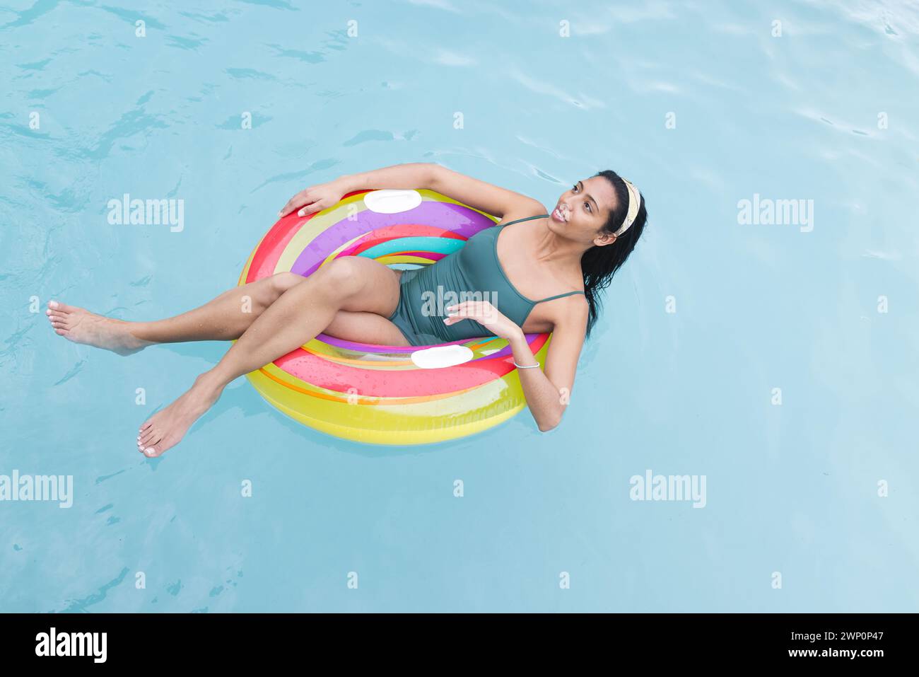 Die junge birassische Frau entspannt sich auf einem farbenfrohen Schwimmbecken, ihre Beine sanft ins Wasser getaucht Stockfoto