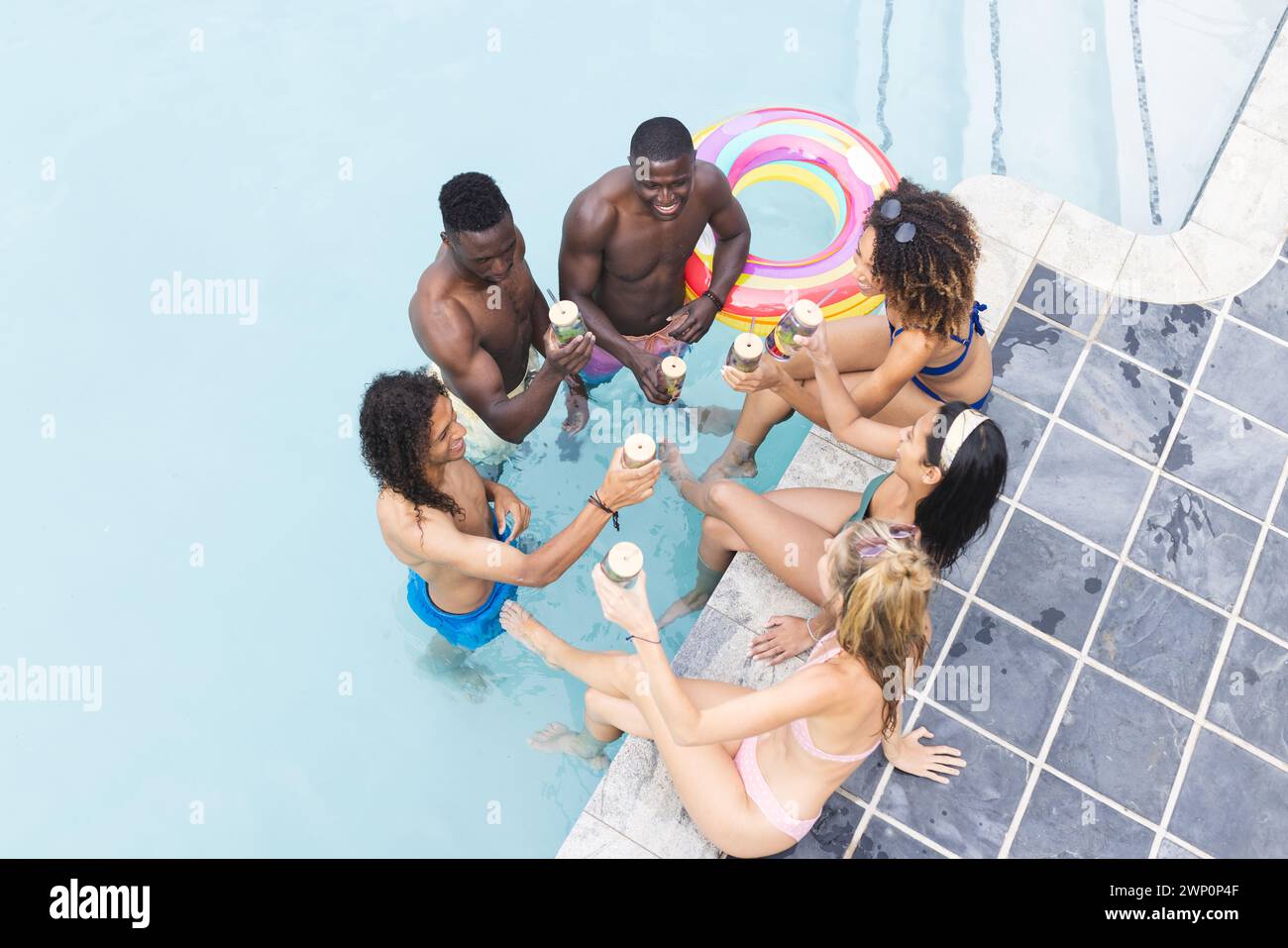 Verschiedene Gruppen von Freunden genießen Getränke am Pool, mit einem farbenfrohen Schwimmer in der Nähe Stockfoto