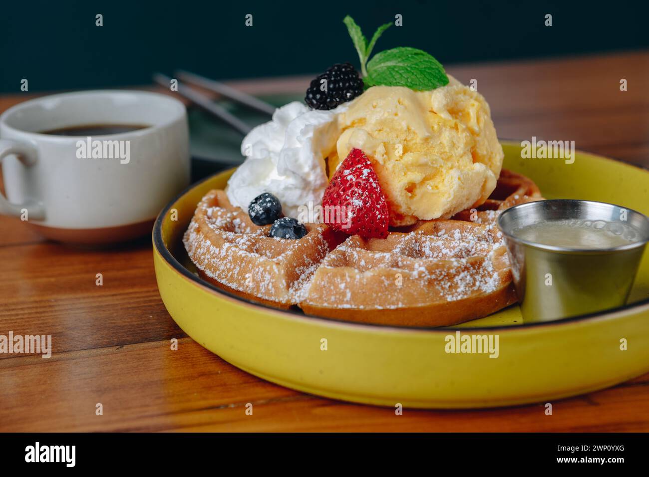 Ein Teller mit Waffeln mit Schlagsahne und Erdbeeren auf einem Tisch neben einer Tasse Kaffee Stockfoto