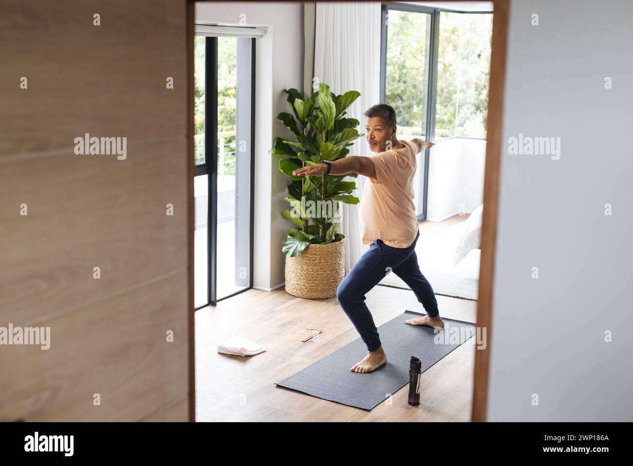 Biracial Senior man übt Yoga in einem hellen, modernen Wohnzimmer mit Kopierraum Stockfoto