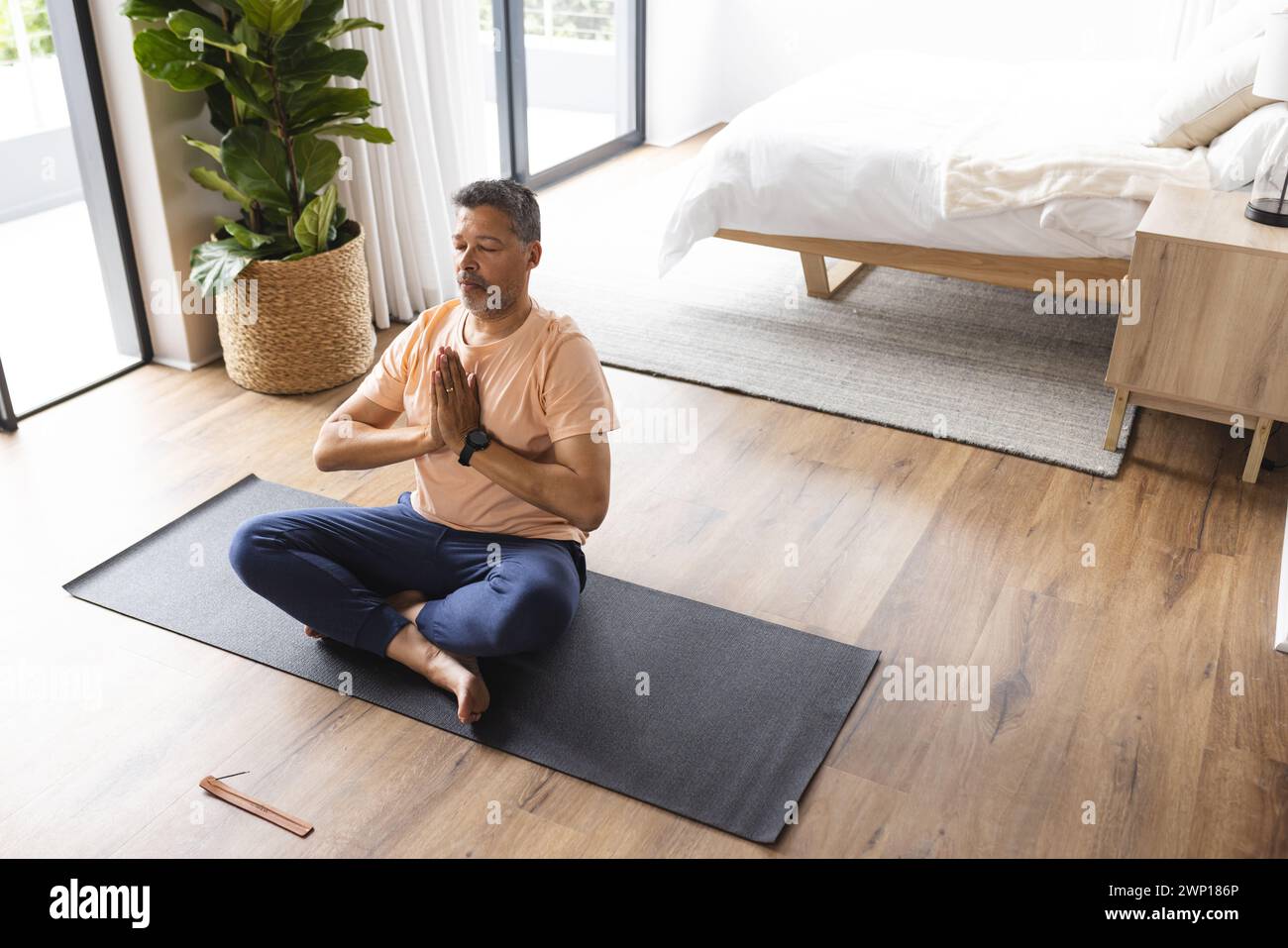 Birassischer Seniorenmann meditiert auf einer Yogamatte in einem hellen Schlafzimmer, mit Kopierraum Stockfoto