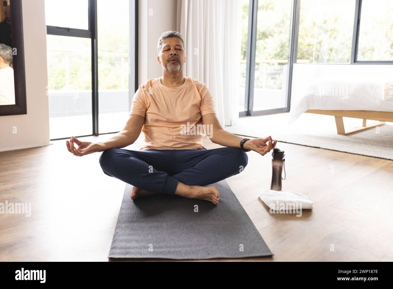 Birassischer Seniorenmann meditiert auf einer Yogamatte in einem hellen Raum Stockfoto
