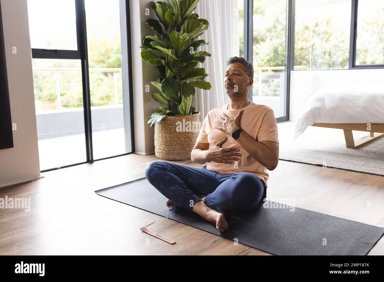Biracial Senior man übt Yoga in einer ruhigen Schlafzimmerumgebung Stockfoto