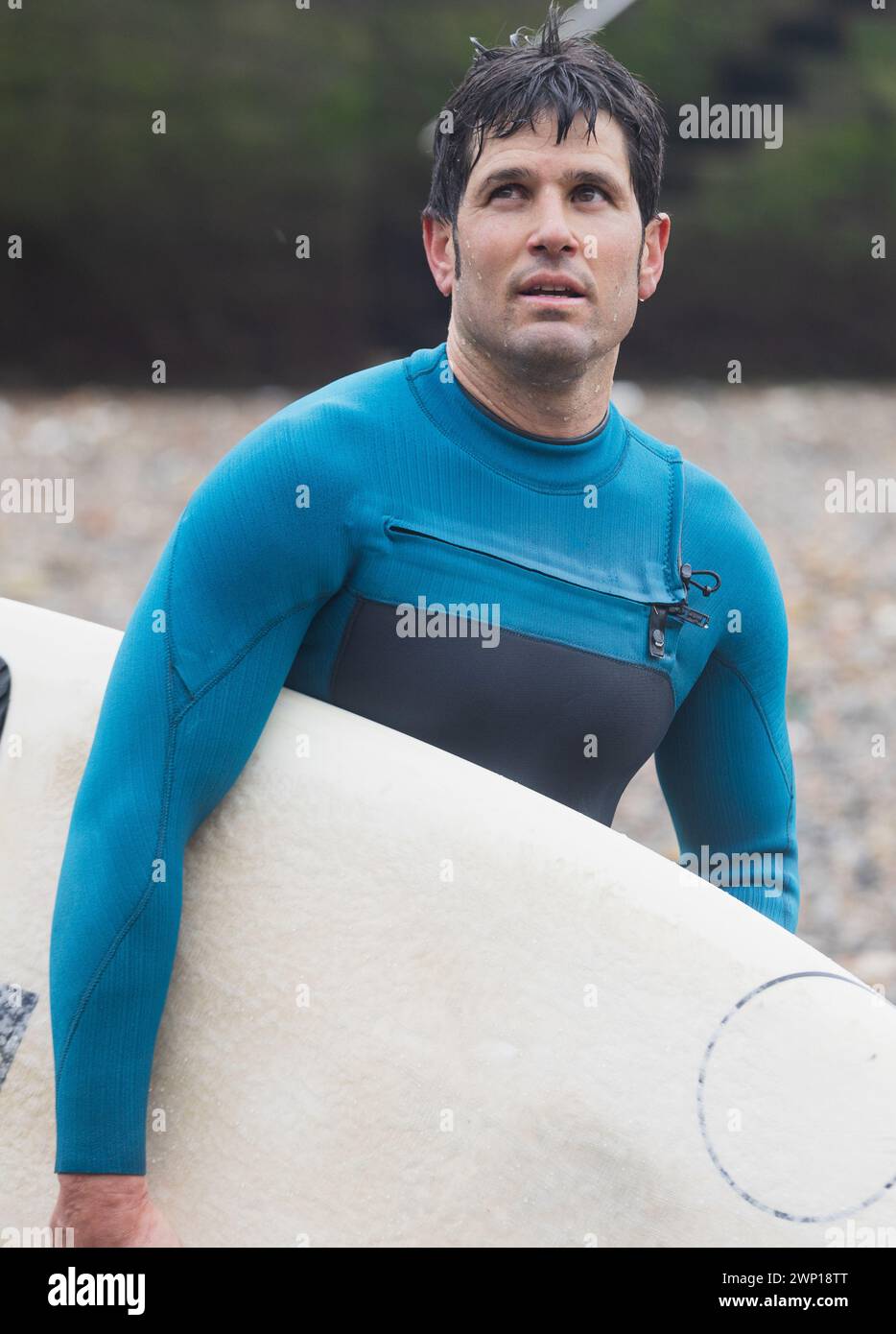Ein Surfer blickt nachdenklich in die Ferne, an Bord in der Hand, am Meer, nachdem er auf den Wellen geritten hat. Stockfoto