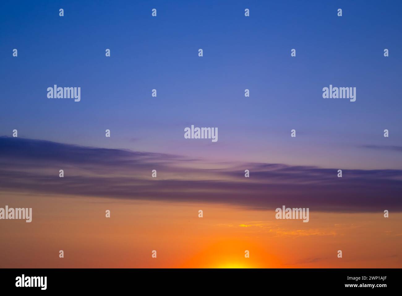 Der wunderschöne Himmel bei Sonnenuntergang ist durch einen Wolkenstreifen in zwei Hälften unterschiedlicher Farben unterteilt. Himmelshintergrund. Stockfoto