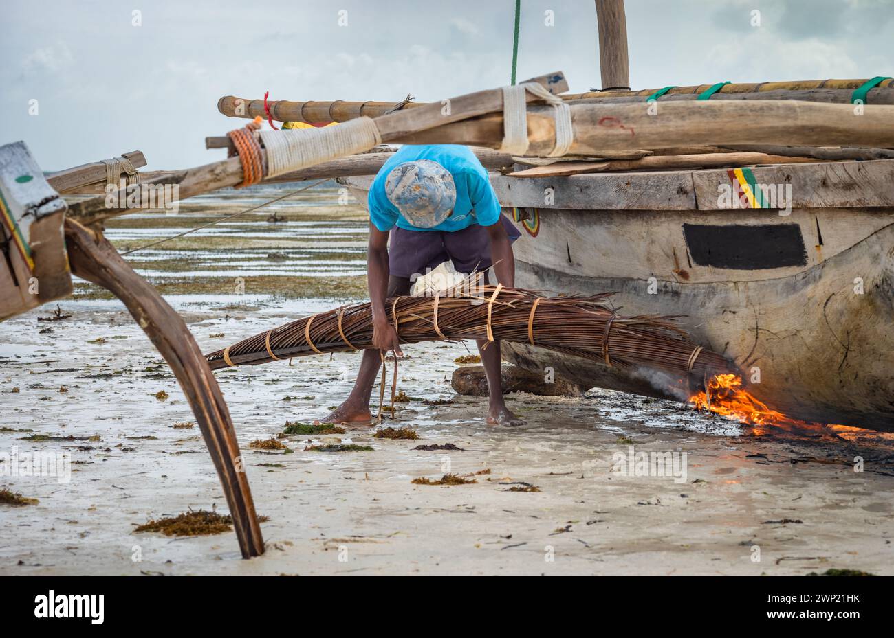 Ein Fischer verwendet brennende Palmenwedel, um den Rumpf seines traditionellen hölzernen Dhow-Bootes Jambiani, Sansibar, Tansania, zu sairieren und zu wasserdicht zu machen Stockfoto