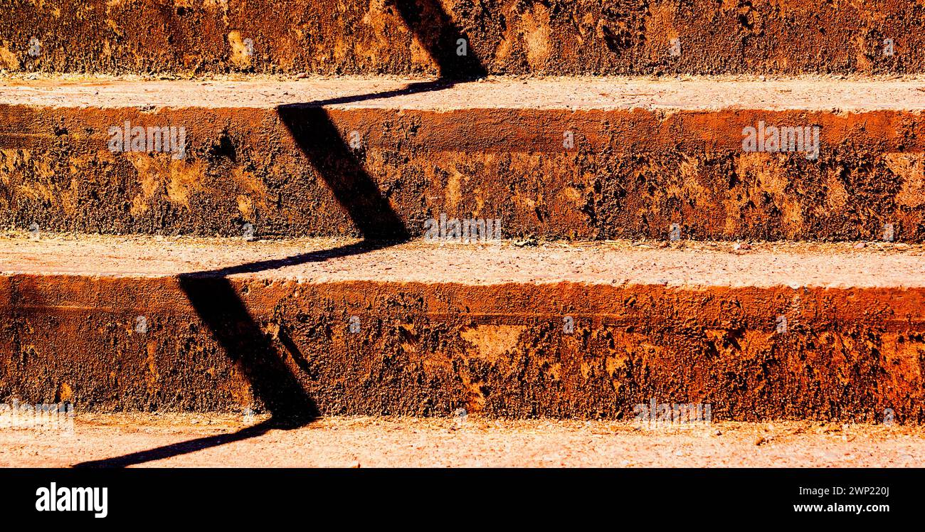Betonstufen, die horizontal orange lackiert sind, mit dunklem ZICKZACK-Schatten vertikal, verursachen optische Verwirrung. Stockfoto