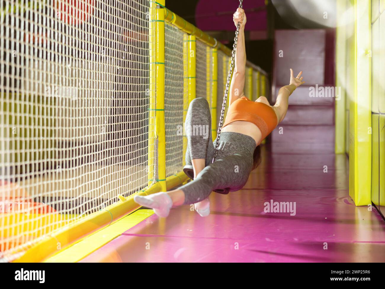 Aufgeregte Frau, die auf der Seilrutsche im modernen Spielzentrum schwingt Stockfoto