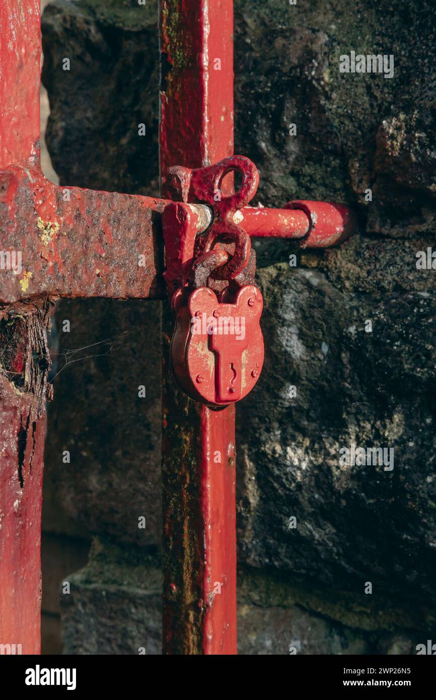 Ein altes rotes Vorhängeschloss an einem Metalltor Stockfoto