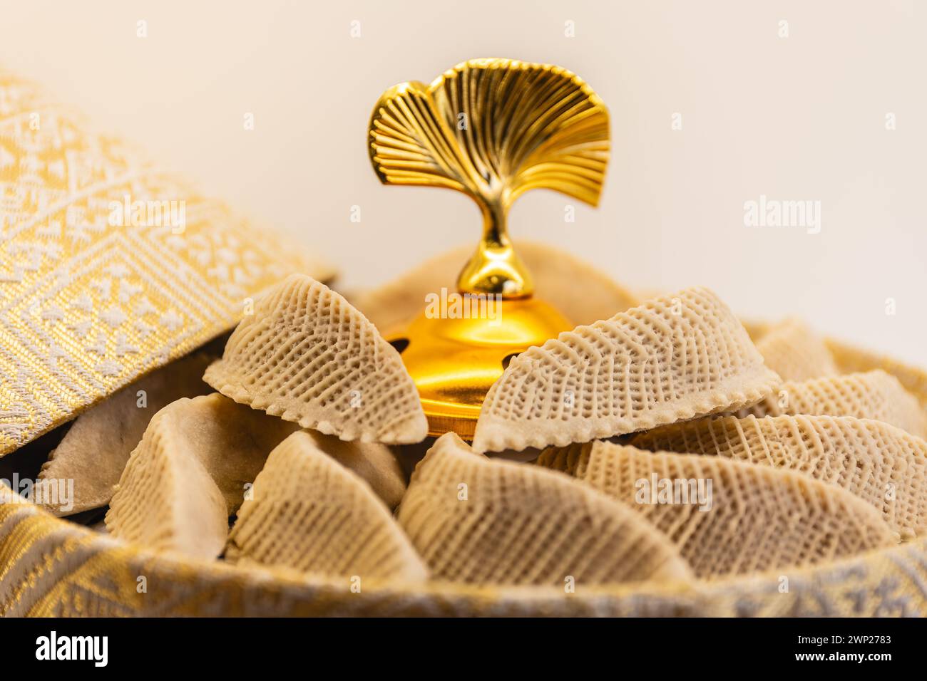 Horizontales Foto ein goldenes Gourmet-Gericht mit einem charakteristischen fächerförmigen Deckel, gefüllt mit zartem, strukturiertem arabischem Gebäck und einem weichen, lila Stockfoto