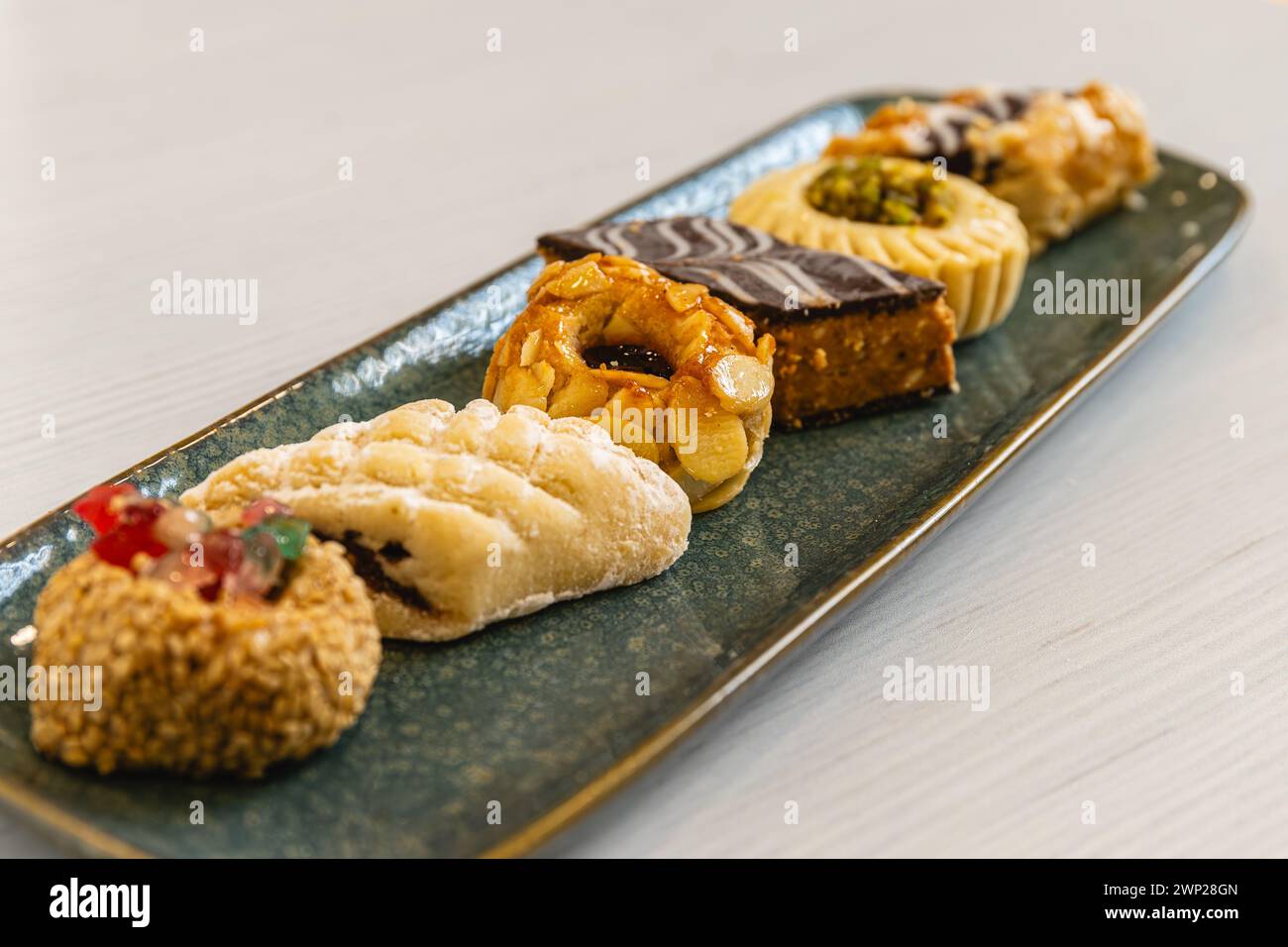 Horizontales Foto ein geschmackvolles Arrangement arabischer Gebäck-Köstlichkeiten mit verschiedenen Belägen, künstlerisch auf einer strukturierten blauen Platte serviert, ideal für h Stockfoto