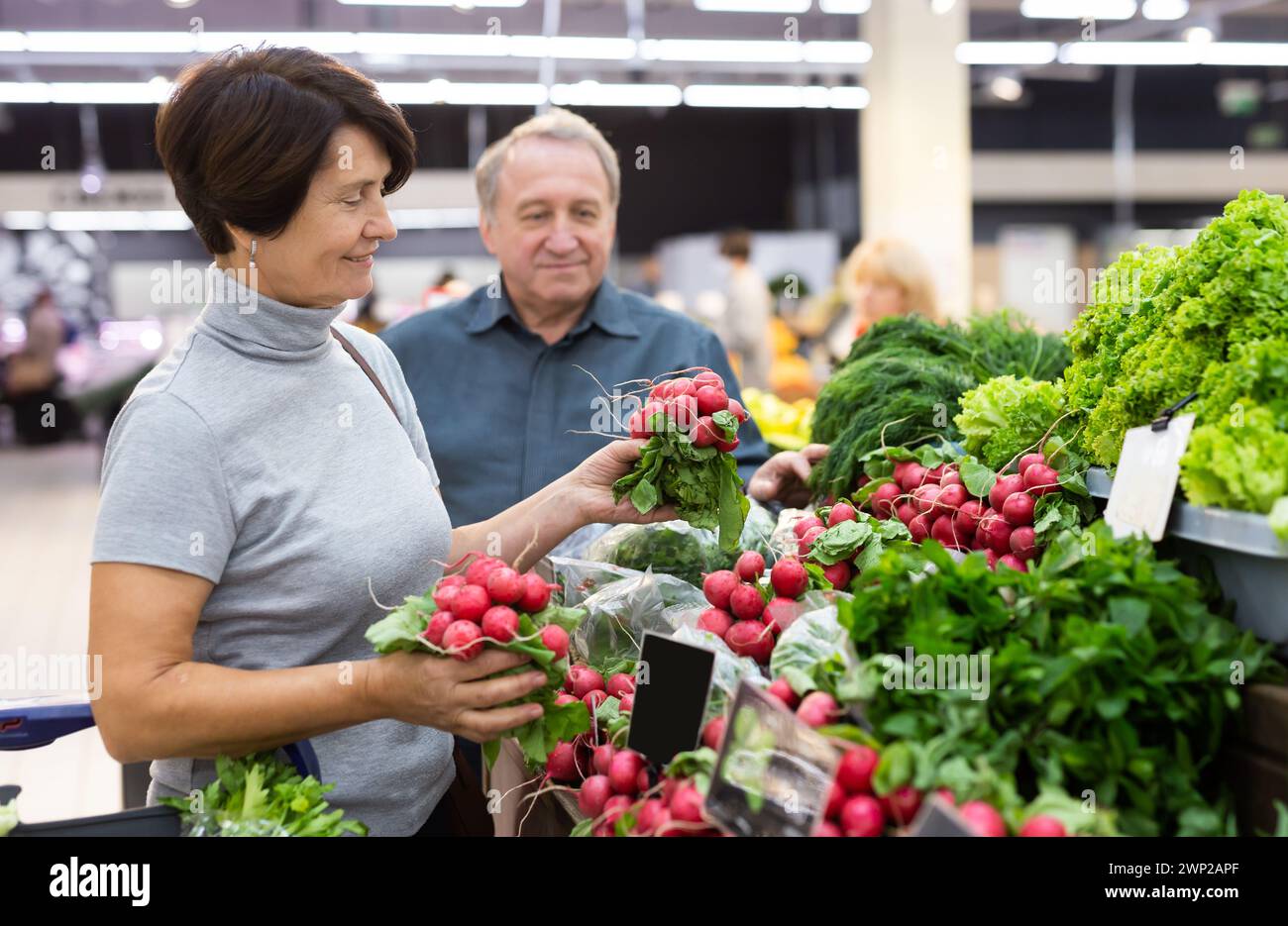 In einem großen Selbstbedienungsladen wählt eine ältere Frau Rettich in der Gemüse- und Obstabteilung Stockfoto