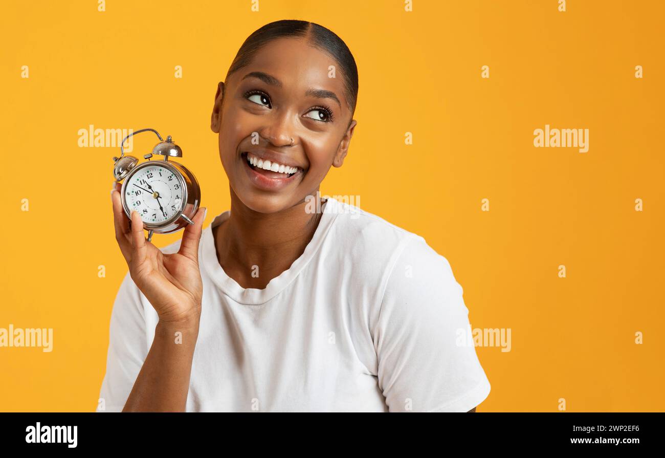 Fröhliche schwarze Millennial-Frau, die Wecker auf gelbem Hintergrund hält Stockfoto