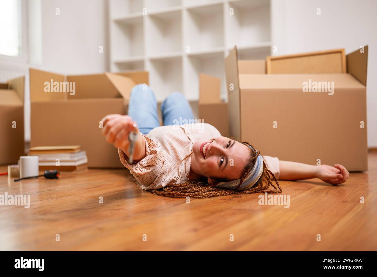 Glückliche Ingwerfrau mit Zöpfen, die den Schlüssel zu ihrem neuen Zuhause halten. Stockfoto