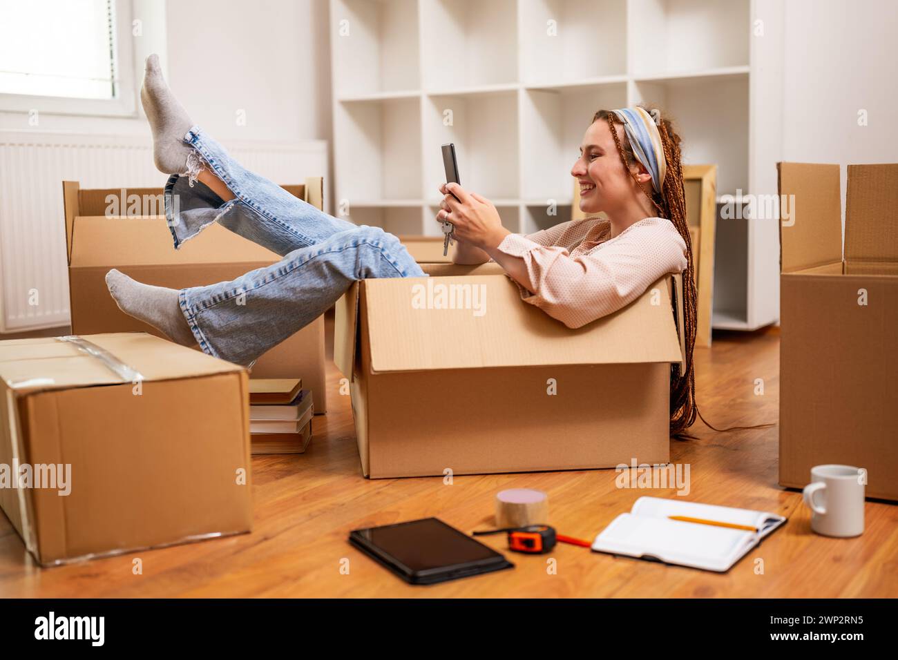 Glückliche Frau, die ein Telefon benutzt und Spaß hat, während sie in eine neue Wohnung zieht. Stockfoto