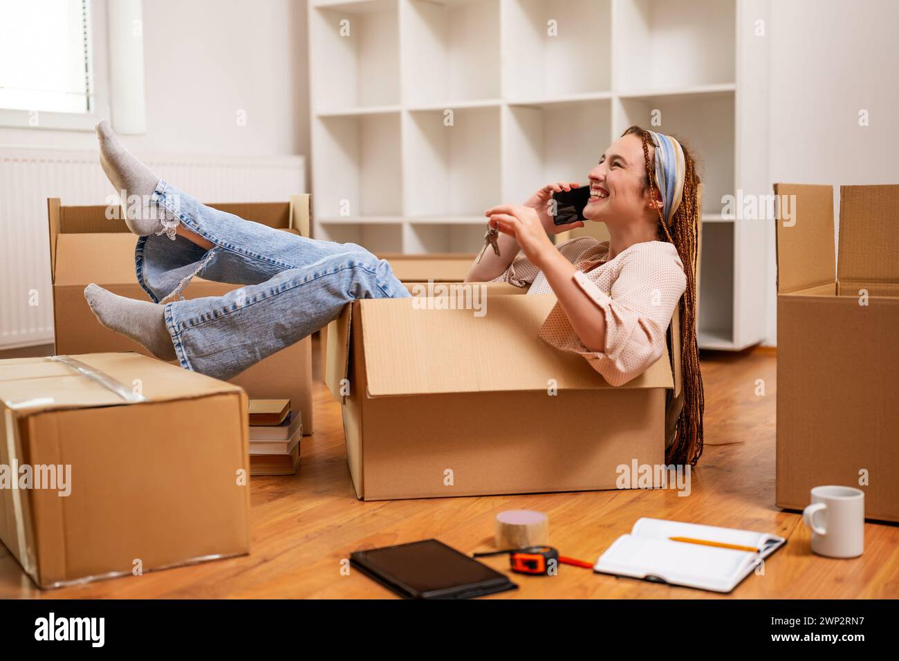 Glückliche Frau, die ein Telefon benutzt und Spaß hat, während sie in eine neue Wohnung zieht. Stockfoto