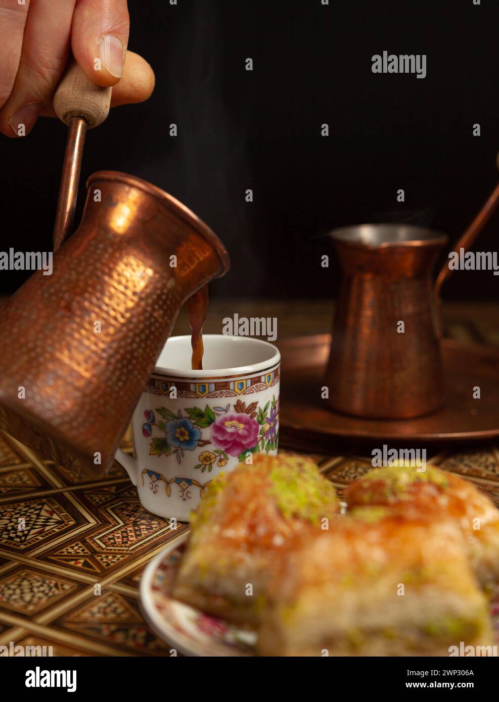 Stillleben mit heißem orientalischem Kaffee, in Zezve gebrüht. Auf dem arabischen Tisch befindet sich eine kleine Kaffeetasse und köstliches Honigbaklava mit Pistazien auf einer Untertasse Stockfoto