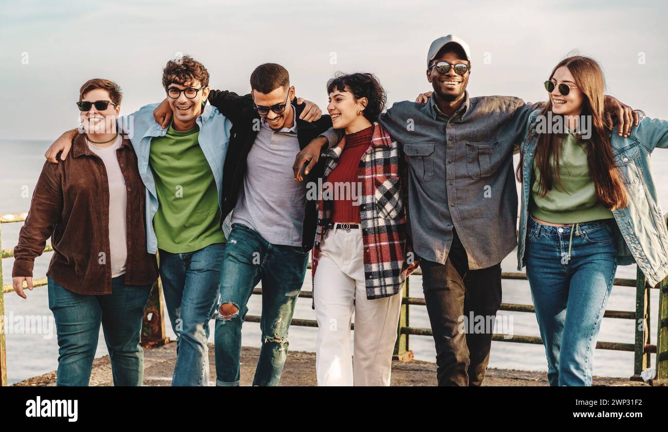 Eine vielfältige Gruppe von Freunden spaziert Arm in Arm und teilt ein Lächeln an einem entspannten Tag. Sie symbolisiert Inklusion und Einheit in lässiger Kleidung Stockfoto