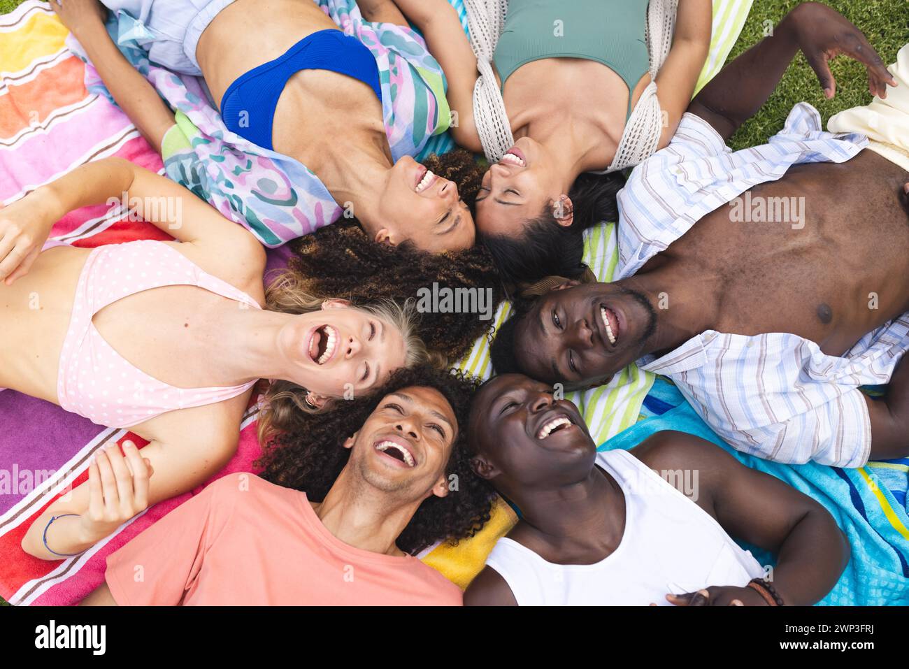 Verschiedene Freunde lachen zusammen, während sie draußen auf einer bunten Decke liegen Stockfoto